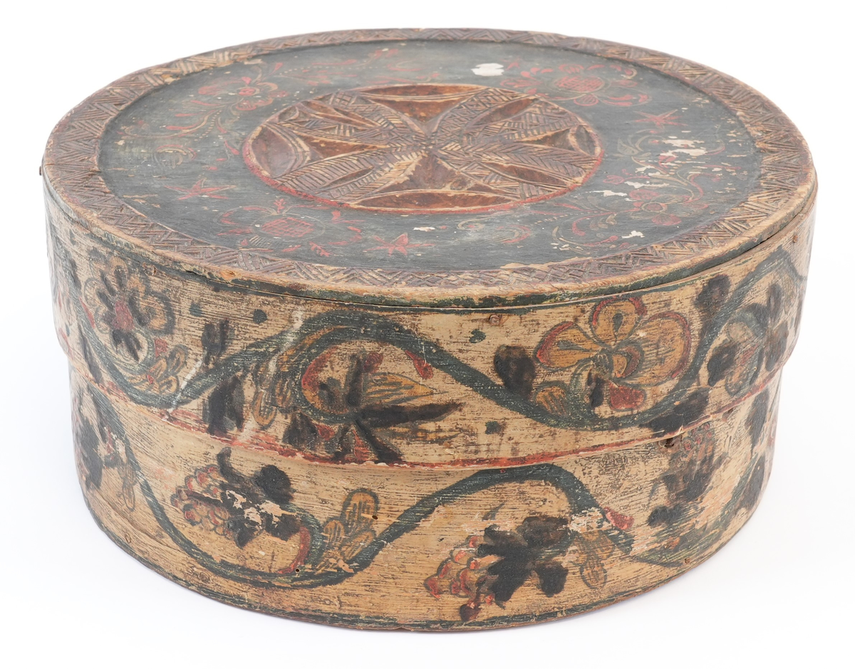 På toppen av lokket karveskurd: i midten utskore eit stort, sentralt buekors med rutenett og sikksakk inni; langs kanten utskoren sikksakk. Mellom dei, på mørkegrøn bakgrunn måla raude og gule blomstrar og slynger. På sideveggen, på kvit bakgrunn måla grøne rankar med raude og gule blomstrar og drueklasar. Innvendig restar av blå målingslaget: på lokket synleg blomsterform, på botnen s-ar.