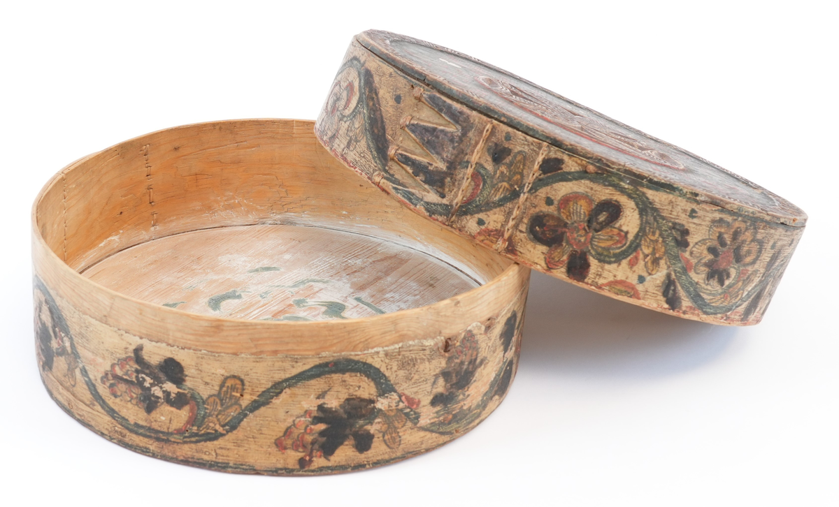 På toppen av lokket karveskurd: i midten utskore eit stort, sentralt buekors med rutenett og sikksakk inni; langs kanten utskoren sikksakk. Mellom dei, på mørkegrøn bakgrunn måla raude og gule blomstrar og slynger. På sideveggen, på kvit bakgrunn måla grøne rankar med raude og gule blomstrar og drueklasar. Innvendig restar av blå målingslaget: på lokket synleg blomsterform, på botnen s-ar.