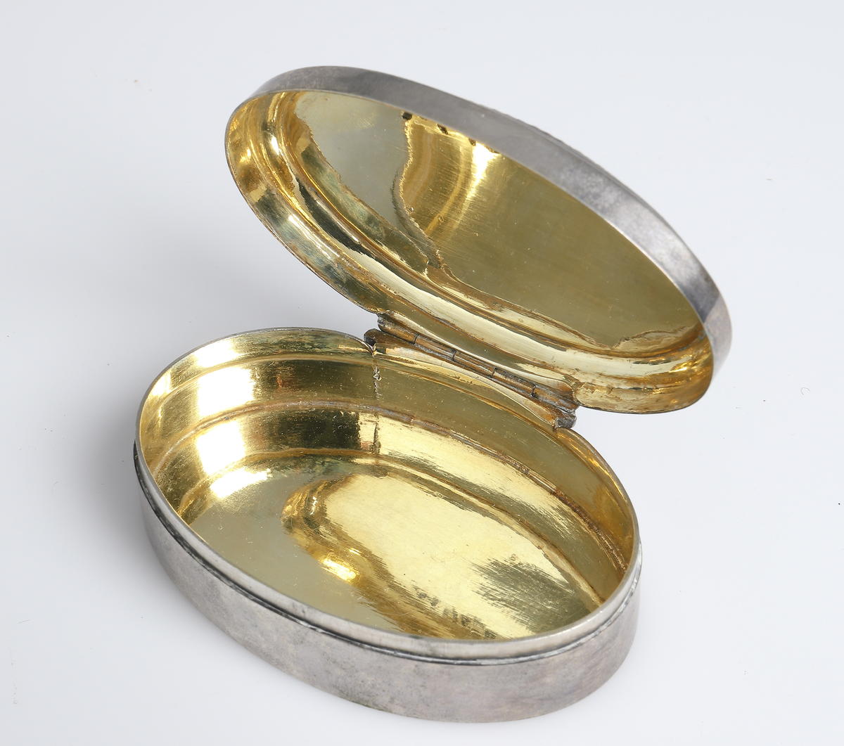 Dosa av silver, med lockOval modell, invändigt förgylld. Locket är försett med filigransarbete som har infattade blå och röda glasflusser. Stämplar i bottnens utsida. Stadsstämpel saknas.

Inskrivet i huvudbok 1988.
