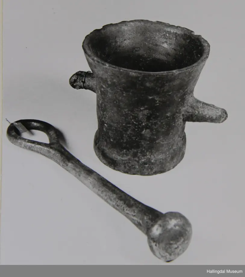 Kopp med tjukke, ujamne, utoverskrånande sider. 2 handtak tvers over kvarandre. Koppen har sirkulært tverrsnitt. Stamp med sirkulært tverrsnitt. Øvst ei stor hempe. Nedst er stampen utvida til ei halvkule.