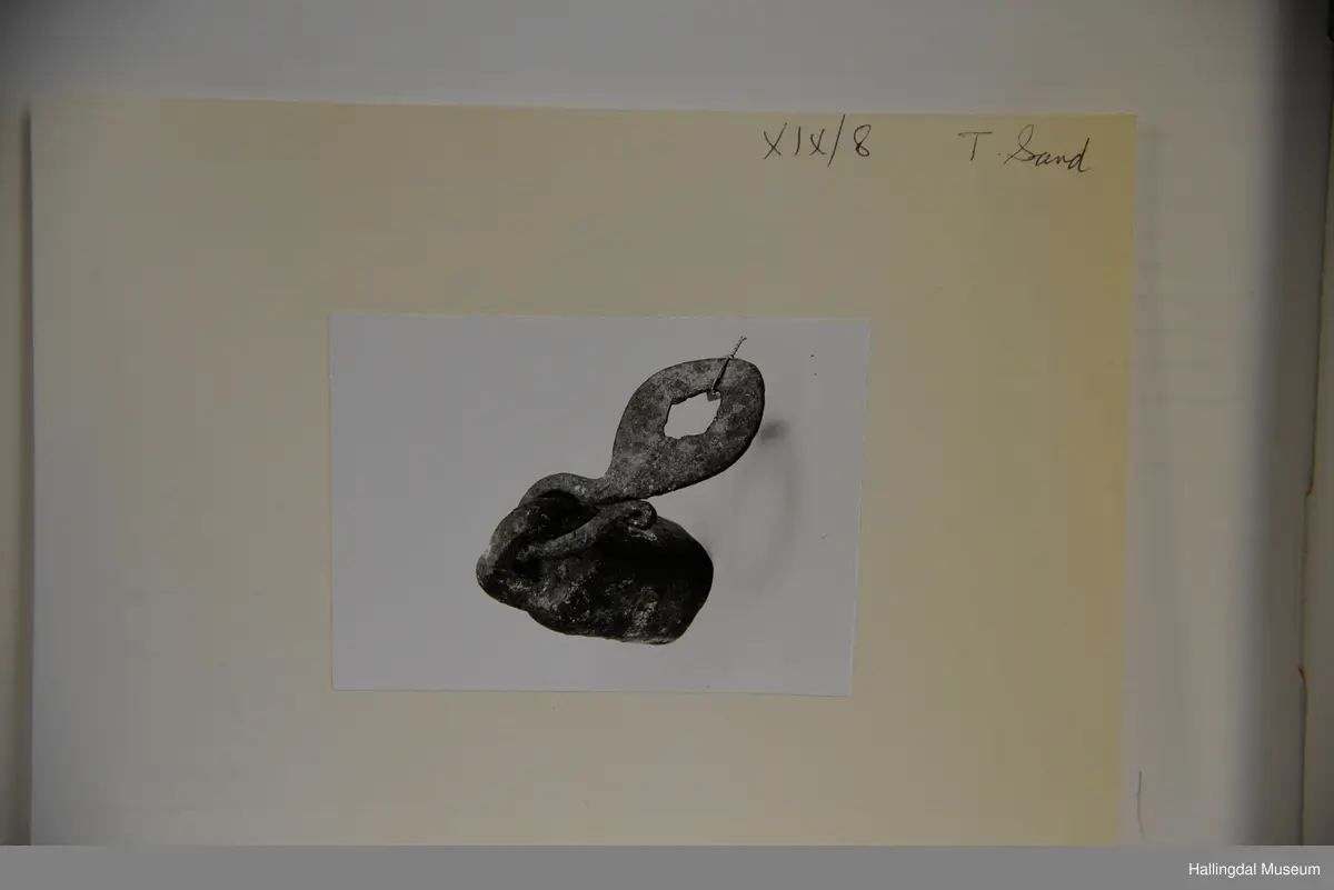 Lodd til å vega med. Rektangulært tverrsnitt. Øvst lodda fast ei stor hempe. I denne hempa festa ein jarnkrok som er opprulla i eine enden og i hin enden har eit flatt, ovalt jarnstykke med hol.