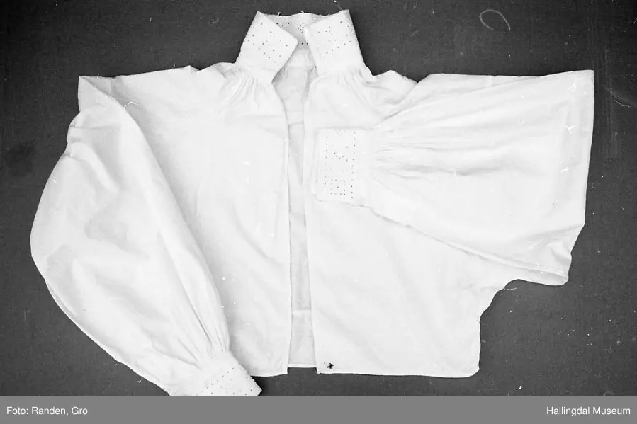 Kvit skjorte med opning framme. Hals- og ermelinningar er brodert i kvitsaum. 