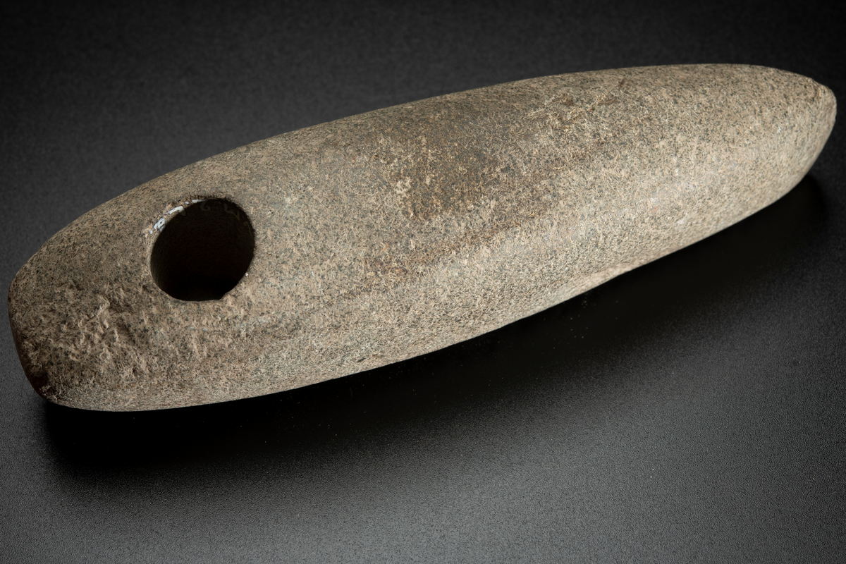 Skafthålsyxa av en ljus, relativt finkornig bergart, möjligen grönsten. Lång och ovanligt smal. Skafthålet placerat långt bakåt. Slipad.