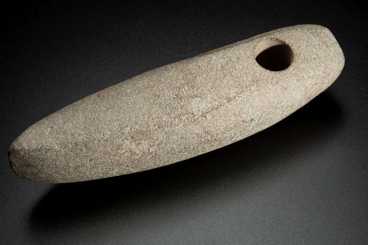 Skafthålsyxa av en ljus, relativt finkornig bergart, möjligen grönsten. Lång och ovanligt smal. Skafthålet placerat långt bakåt. Slipad.