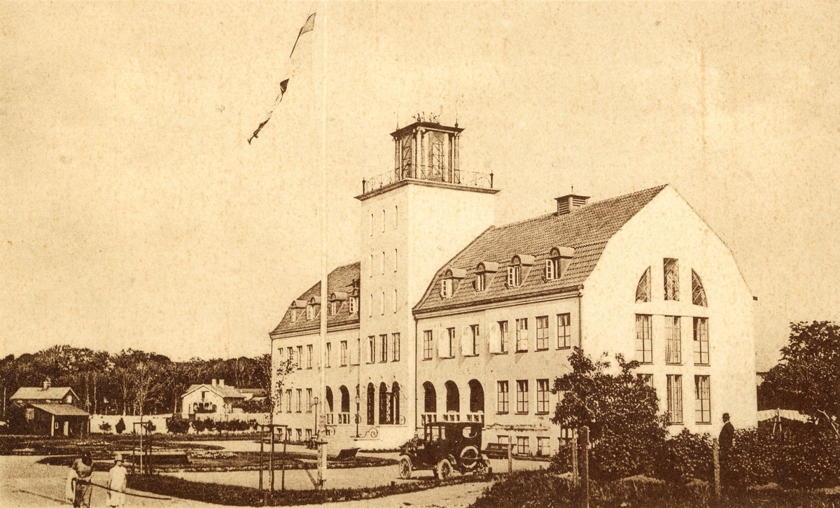 Vykort, två olika versioner av samma fotografi föreställande Varbergs nya varmbadhus, som stod klart 1925. Det äldre från 1866 låg nere vid vattnet, medan detta förlades vid Strandgatan. En bil står parkerad framför badhuset. Kvarteret hette då Styrmannen men uppgår numera i kv Skepparen. (Se även bildnr F1673.)