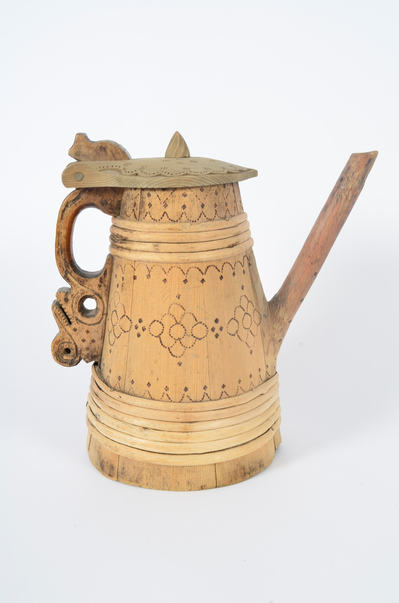 Kanne lagget av åtte staver som smalner opp. Tut og hank i ett med hver sin stav. Nederst seks gjorder og fire øverst. Lokket er buet med kjegleformet topp, ender i nebb og er festet til hanken med trepinne. Hanken nederst har opp-ned slangehode. Sviornamentikk på både kanne og lokk. Lokket er av nyere dato.