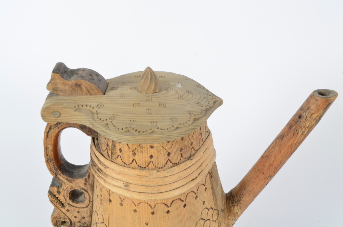 Kanne lagget av åtte staver som smalner opp. Tut og hank i ett med hver sin stav. Nederst seks gjorder og fire øverst. Lokket er buet med kjegleformet topp, ender i nebb og er festet til hanken med trepinne. Hanken nederst har opp-ned slangehode. Sviornamentikk på både kanne og lokk. Lokket er av nyere dato.