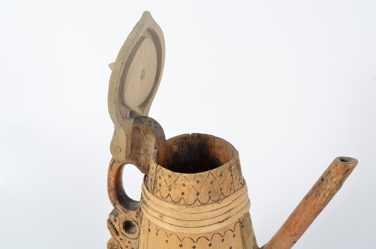 Kanne lagget av åtte staver som smalner opp. Tut og hank i ett med hver sin stav. Nederst seks gjorder og fire øverst. Lokket er buet med kjegleformet topp, ender i nebb og er festet til hanken med trepinne. Hanken nederst har opp-ned slangehode. Sviornamentikk på både kanne og lokk. Lokket er av nyere dato.