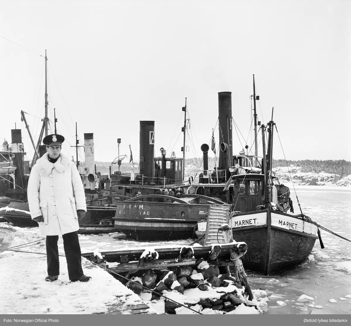 Slepebåtene fra Østfold er vel framme i Sverige etter slepebåtaksjonen 8. februar 1945. 
Slepebåten Fram av Fredrikstad til høyre for svensk politivakt, deretter slepebåten Marnet av Fredrikstad. Bak politivakt er slepebåten Oscarsborg. 


Tekstseddel limt på bakside av positiv:
NORWEGIAN OFFICIAL PHOTO NO. S. 5569. 
NORSK FLÅTE FØRT TIL SVERIGE.
"Bevepnede menn satte seg torsdag den 8. februar 1945 i besittelse av Fredrikstads hele flåte av slepebåter og dirigerte den til Sverige, ialt 11. Samtidig ble bergingsbåten "Uredd" som var stasjonert i Moss, dirigert samme vei. Alle disse båter arbeidet for tysk regning med å bugsere fartøyer til ppg fra Fredrikstad,  som er bllitt en stor utskipingshavn for tyskerne. 
Det store kuppet foregikk på den måten at vepnede folk gikk ombord på båtene og overmannet mannskapene. Tre slepebåter som ikke hadde dampen oppe, ble senket på havnen. Kuppet var vel organisert. De kaprende mannskaper gikk ombord i de båter som lå ved kai, og disse båtene ble så styrt bort til de andre som i sin tur fikk kapringsmannskaper ombord. Båtenes kapteiner fikk valget mellom å styre etter ordreeller gå under dekk. En av båtene som skulle  i tyske tjeneste den dagen ble  entret kl. 7.30 om morgenen, og den utførte hele dagen sin slepning av tyske skyteskiver. Først da skyteøvelsene var ferdig, stakk den til Sverige. De andre fartøyer foretok ferden til Sverige i samlet følge.. 
Bildet viser båtene i svensk havn. I forgrunnen svensk politivakt.
Stockholm 22. 2.45."
