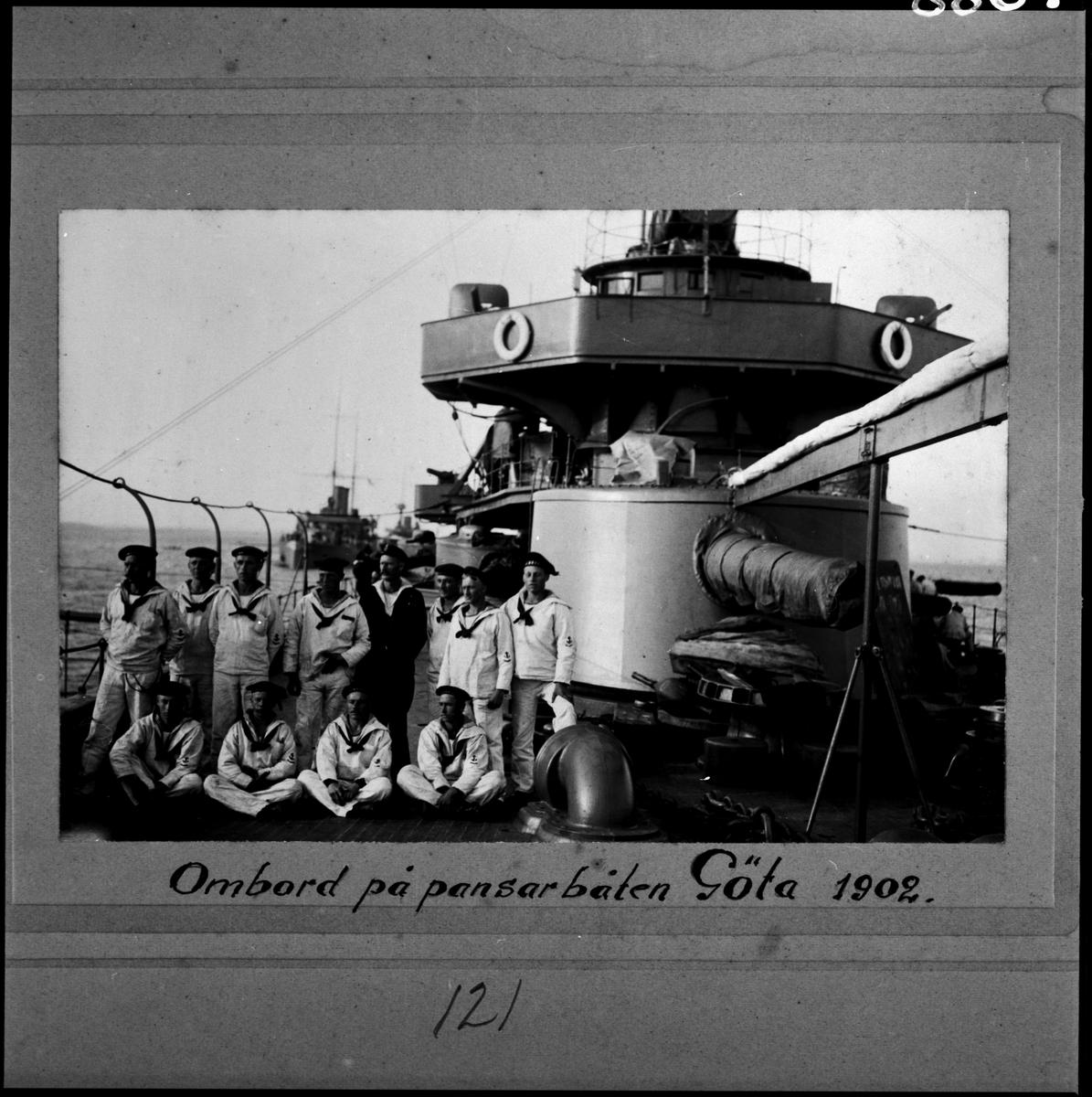 Denna grupporträtt föreställer manskap kläd i vita sjömanskostymer ombord på pansarbåten Göta 1902.