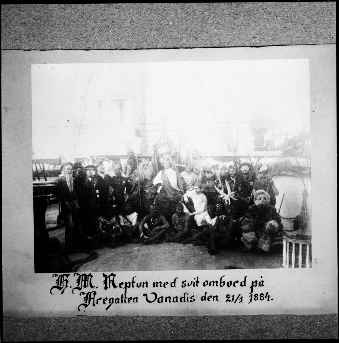 Bilden föreställer en grupp fantasifull utklädda sjömän som har samlats på däck inför neptunifesten vid passerandet av linjen 21/1 1884 ombord på fregatten Vanadis världsomsegling 1883-85.