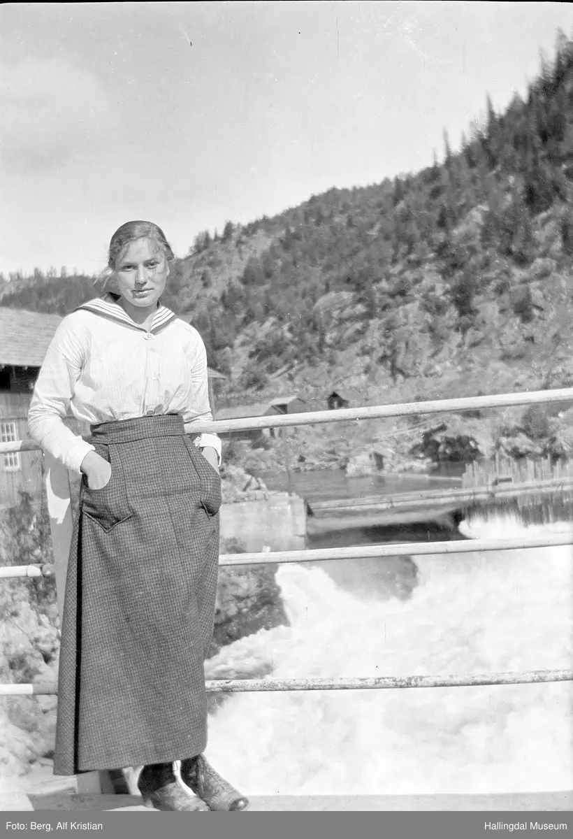 Ragna Berg f. Kolsrud står på brua ved Storebrufossen i Bagn i Valdres. Elva er Begna. Informant er Kåre Leite.
