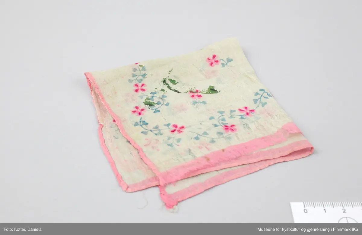 Tørkleet er nærmest kvadratisk og er laget mest sannsynlig av silke. Sett under mikroskopet, har trådene en relativ glatt overflate og en naturhvitt til beige farge. Veft (innslaget) og varpene (renningen) består av like mange enkelttråder, anslagsvis 10 stykk. Blomstermønsteret er påtrykt med ulike fargestoffer i lyseblå, lyserosa og mørkere rosa. Kantene er sydd om med maskinsøm, unntatt en side der sømmen er borte.
Tørkleet påviser grønne flekker av en form for limstoff, som er det samme som på en relatert gjenstand, en brosje laget av en russefange. Begge gjenstander ble oppbevart sammen i lang tid.