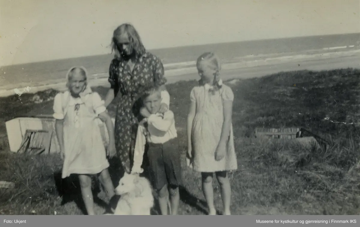 En ung kvinne står, sammen med to jenter, en gutt og en hund i sanddynene. I bakgrunnen ser man strand og hav.  Bildet er tatt i Nordjylland i Danmark og viser Kari Wulff som 10- eller 11-åring, helt til venstre. Den unge kvinnen som holder henne ved armen heter Lis og er storesøsteren til Ida til høyre i bildet. Disse to er døtrene til pleiemora Wanda Nielsen. Gutten heter Tore, er 6 år gammel og jentenes fetter. Jentene er kledd i sommerkjoler, Tore har på seg et langarmet skjorte og knelange bukser med bukseseler. Foran dem sitter en hund som Tore holder fast ved halsbåndet.