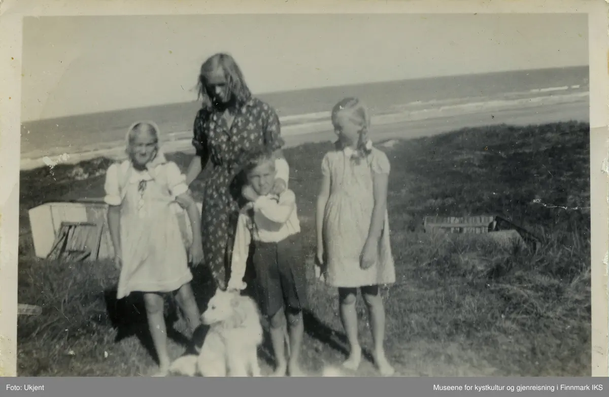 En ung kvinne står, sammen med to jenter, en gutt og en hund i sanddynene. I bakgrunnen ser man strand og hav.  Bildet er tatt i Nordjylland i Danmark og viser Kari Wulff som 10- eller 11-åring, helt til venstre. Den unge kvinnen som holder henne ved armen heter Lis og er storesøsteren til Ida til høyre i bildet. Disse to er døtrene til pleiemora Wanda Nielsen. Gutten heter Tore, er 6 år gammel og jentenes fetter. Jentene er kledd i sommerkjoler, Tore har på seg et langarmet skjorte og knelange bukser med bukseseler. Foran dem sitter en hund som Tore holder fast ved halsbåndet.