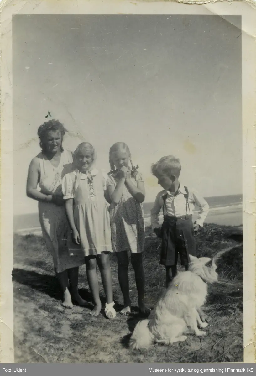 En kvinne står med to jenter og en gutt i sanddynene. De har en hund med seg. Bak dem ser man strand og hav. Personene er ikledd sommerklær, kvinnen og jentene i kjoler, gutten i langarmet skjørt og knelange bukser med bukseseler. 
Kvinnen som er avbildet heter Wanda Nielsen, er dansk og tok imot norske Kari Wulff fra Hammerfest til et ferieopphold i sommeren 1945. Kari, den gang 10 eller 11 år gammel, er andre person fra venstre i bildet. Hun har et skaut på hodet og hennes venstre fot er bandasjert. Jenta ved siden av Kari er danske Ida, datteren til Wanda, og lengst til høyre i bildet ser man Tore, også han dansk og fetter til Ida.