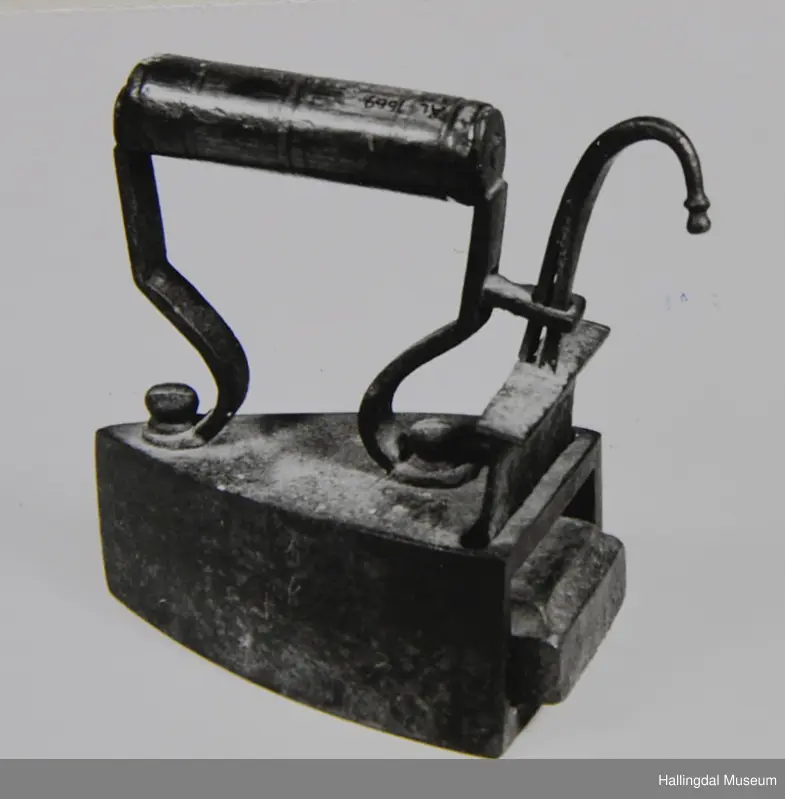 Tre loddrette sider, dei to langsidene noko krumma, stuttsida rett med opning til bolt. Over- og undersida flat. På oversida eit rektangulært hol på den bakre delen. I holet ei jarnplate med stang med bøygd krok øvst midt på. Denne jarnplate tener som lem for bolten som er fastrusta inni strykejarnet. Sylindrisk dreia handtak.