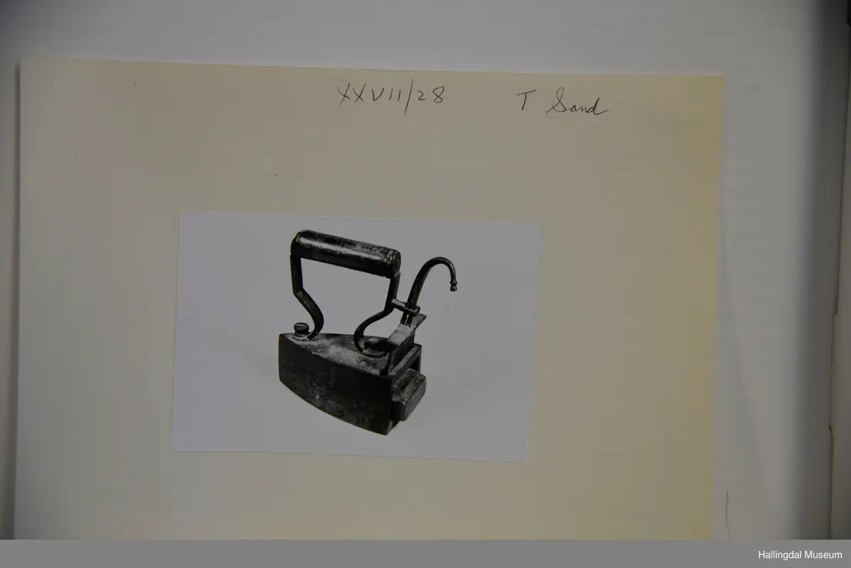 Tre loddrette sider, dei to langsidene noko krumma, stuttsida rett med opning til bolt. Over- og undersida flat. På oversida eit rektangulært hol på den bakre delen. I holet ei jarnplate med stang med bøygd krok øvst midt på. Denne jarnplate tener som lem for bolten som er fastrusta inni strykejarnet. Sylindrisk dreia handtak.