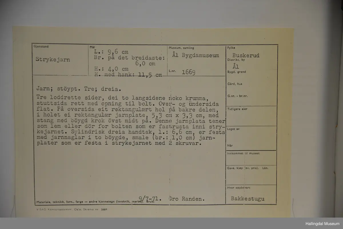 Tre loddrette sider, dei to langsidene noko krumma, stuttsida rett med opning til bolt. Over- og undersida flat. På oversida eit rektangulært hol på den bakre delen. I holet ei jarnplate med stang med bøygd krok øvst midt på. Denne jarnplate tener som lem for bolten som er fastrusta inni strykejarnet. Sylindrisk dreia handtak.