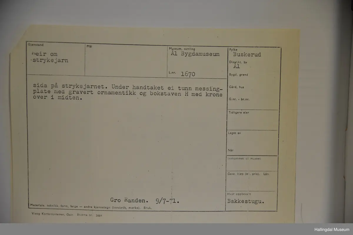 Strykejarn støypt i jarn og med dreia hank. Oversida er eit lok for å kunne putte glør i strykejarnet. Under handtaket ei tunn messingplate med gravert ornamentikk og bokstaven H med krone over i midten.