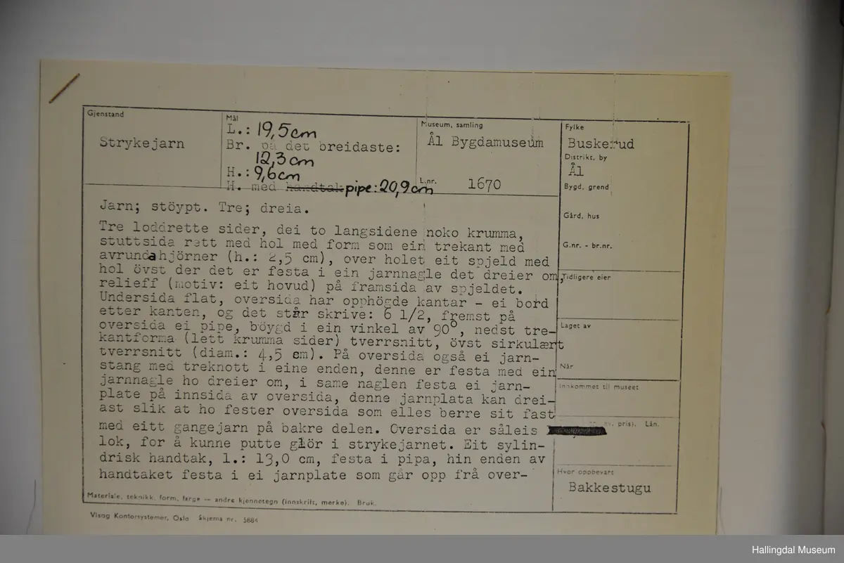 Strykejarn støypt i jarn og med dreia hank. Oversida er eit lok for å kunne putte glør i strykejarnet. Under handtaket ei tunn messingplate med gravert ornamentikk og bokstaven H med krone over i midten.