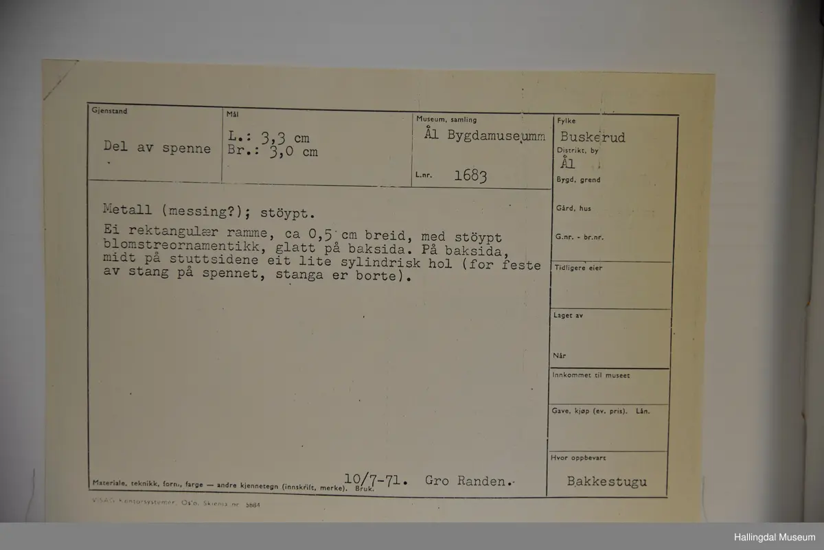 Del av spenne i messing (?). Rektangulær ramme, støypt blomsterornamentikkk, glatt på baksida. Stanga er borte.