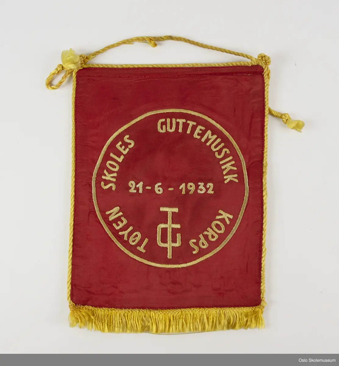 Rektangulær vimpel med gul kant og frynser. Den ene siden av vimplene er rød med gul/hvit brodert dekor. Den andre siden er hvit med tre broderte blåklokker og noter.