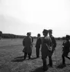 Kamratmötet, I 11. Ett antal herrar i uniform och några civila, står och pratar på övningsfältet.