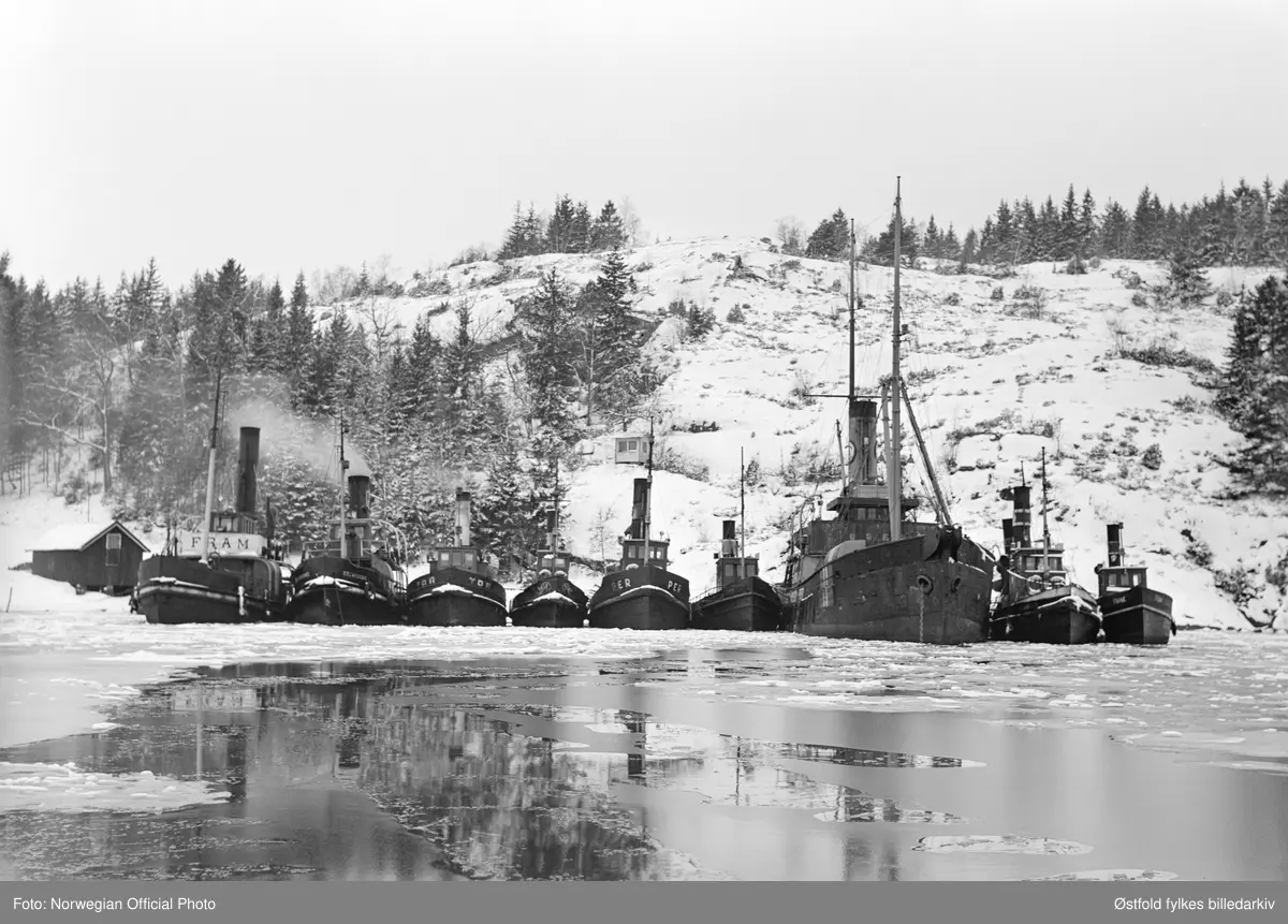 Slepebåtene fra Østfold er vel framme i Sverige etter slepebåtaksjonen 8. februar 1945. Fra venstre slepebåtene Fram, Oscarsborg, Tor, Fix, Per og NN, Uræd/Uredd, og NN, NN?

Tekstseddel limt på bakside av positiv:
NORWEGIAN OFFICIAL PHOTO NO. S. 5568. 
NORSK FLÅTE FØRT TIL SVERIGE.
"Bevepnede menn satte seg torsdag den 8. februar 1945 i besittelse av Fredrikstads hele flåte av slepebåter og dirigerte den til Sverige, ialt 11. Samtidig ble bergingsbåten "Uredd" som var stasjonert i Moss, dirigert samme vei. Alle disse båter arbeidet for tysk regning med å bugsere fartøyer til ppg fra Fredrikstad,  som er bllitt en stor utskipingshavn for tyskerne. 
Det store kuppet foregikk på den måten at vepnede folk gikk ombord på båtene og overmannet mannskapene. Tre slepebåter som ikke hadde dampen oppe, ble senket på havnen. Kuppet var vel organisert. De kaprende mannskaper gikk ombord i de båter som lå ved kai, og disse båtene ble så styrt bort til de andre som i sin tur fikk kapringsmannskaper ombord. Båtenes kapteiner fikk valget mellom å styre etter ordreeller gå under dekk. En av båtene som skulle  i tyske tjeneste den dagen ble  entret kl. 7.30 om morgenen, og den utførte hele dagen sin slepning av tyske skyteskiver. Først da skyteøvelsene var ferdig, stakk den til Sverige. De andre fartøyer foretok ferden til Sverige i samlet følge.. 
Bildet viser slepebåtene trygt i en svensk havn. 
Stockholm 22. 2.45."