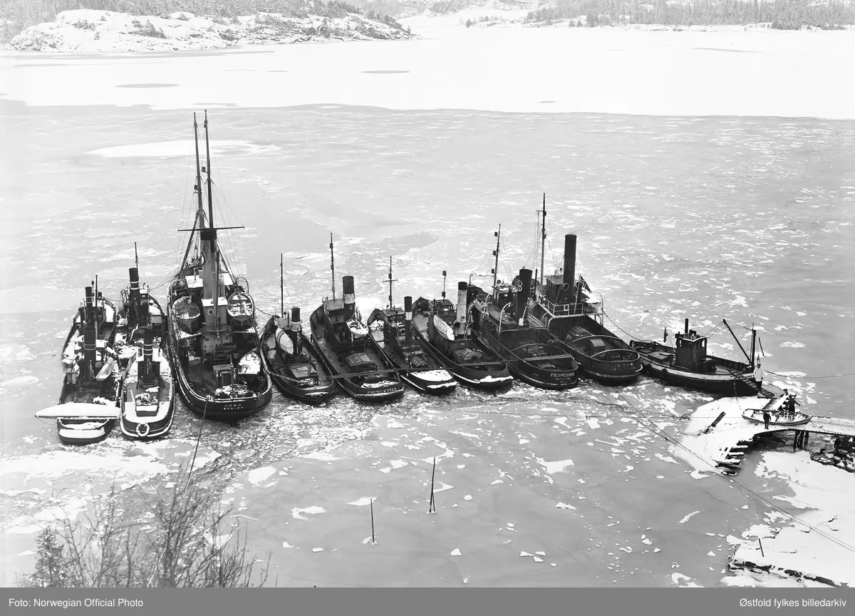 Slepebåtene fra Østfold er vel framme i Sverige etter slepebåtaksjonen 8. februar 1945. På bildet i alt 11 slepebåter og en bergingsbåt. På noen av båtene er det menn på dekk. På landgangen til slepebåten Marnet, helt til høyre, står en svensk politivakt. På brygga er det to karer som bukserer en robåt. 

Slepebåtene fra venstre: 
1. 
2.
3. Uræd, Bergen (bergingsbåt)
4. 
5. Per
6. Fix, Fredrikstad
7. Tor, Fredrikstad
8. Oscarsborg, Fredrikstad
9. Fram, Fredrikstad
10. Marnet

Bakerste rad fra venstre: 
1. 
2. 

De øvrige slepebåtene var Lillegutt, Frank, Hedvik, Glimt og Lyr, plassering av disse slepebåtene på bildet er ikke kjent.
 
Tekstseddel limt på bakside av positiv:
NORWEGIAN OFFICIAL PHOTO NO. S. 5568. 
NORSK FLÅTE TIL SVERIGE.
"Vepnede menn satte seg torsdag den 8. februar 1945 i besittelse av Fredrikstads flåte av slepebåter. De 11  slepebåter og bergingsbåten Uredd som var stasjonert i Moss, ble ført til Sverige. Disse båtene arbeidet for tyskerne. Slepebåtene brukes for å bugsere fartøy opp Glomma til Fredrikstad som er en viktig utskipingshavn for tyskerne. 
Kuppet foregikk på den måten av vepnede folk gikk ombord i båtene og overmannet mannskapene. 3 slepebåter som ikke hadde dampen oppe, ble senket på havnen. Kuppet var godt organisert. Kapringsmannskapene gikk ombord i de båtene som lå ved kaien. Disse båtene ble så ført opp til de andre som i sin tur fikk "prisemannskap" ombord. Båtenes kapteiner fikk ordre om å føre sine båter eller gå under dekk. En av båtene skulle om morgenen i tyske tjeneste. Den ble entret kl. 7.30.  Hele dagen slepte den skyteskiver for tyskerne. Da skyteøvelsene var slutt, stakk de til Sverige. De andre båtene gikk samlet til svensk havn. 
Bildet viser slepebåtene trygt i svensk havn. 
Stockholm 22. februar."