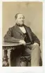 Porträtt av en okänd man, möjligen riksdagsman, sittande på en stol.