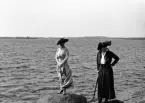 Några sommarklädda kvinnor står på några stenar vid havet.