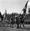 Medborgartåget, 16/6 1940. Fanborg på Värendsvallen. Två scouter och två män klädda i militäruniform går i täten, framför ett antal kvinnor, klädda i s.k. husmorsdräkt.
