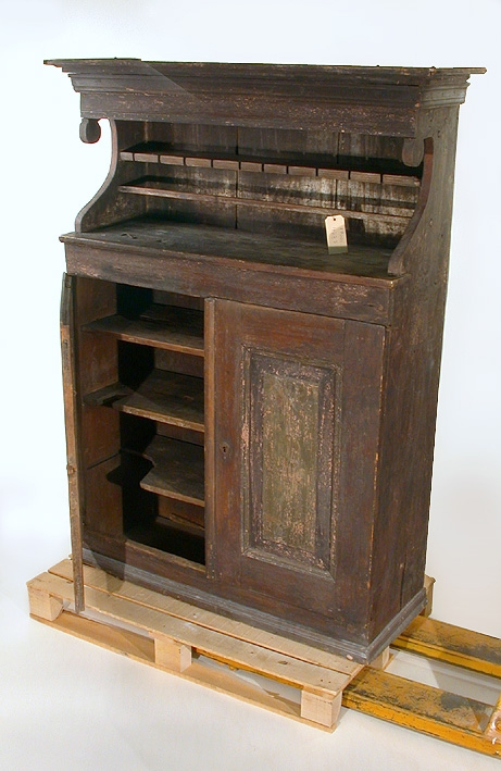 Träskåp med dubbeldörrar nedtill innehållande tre hyllor. Målade men ej ornerade dörrspeglar. Upptill öppen med en hylla samt en trälist. Uttag för att hänga bestick ifrån. Takformat krön.