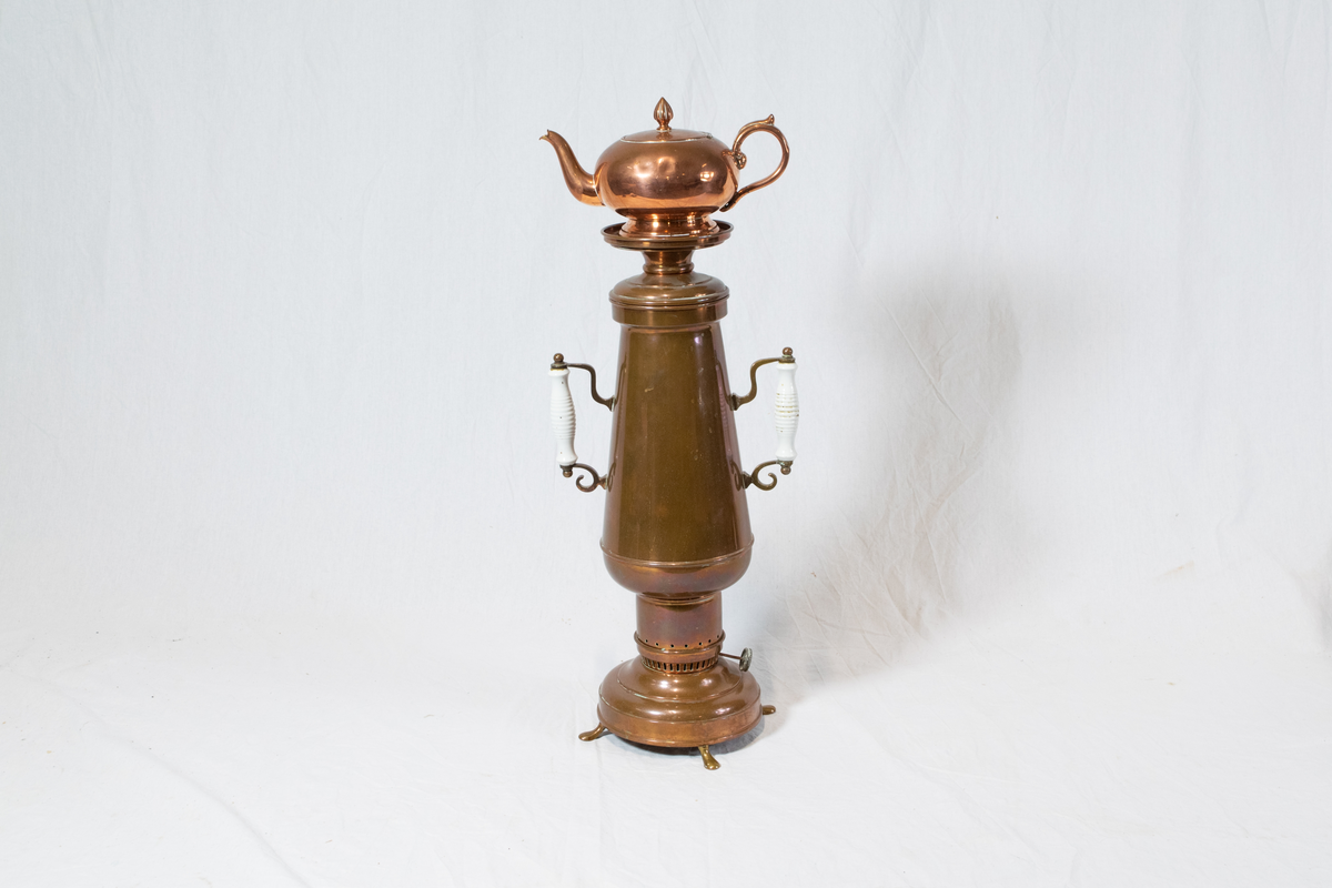 Samovar i messing. Består av fire deler. Beholder/kolbe med justering til bluss med hvite håndtak, en kanne på toppen og to mellomdeler mellom kanne og kolbe.