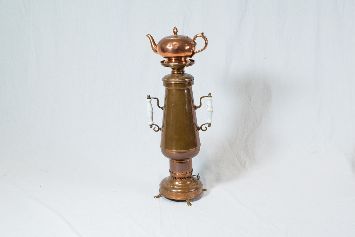 Samovar i messing. Består av fire deler. Beholder/kolbe med justering til bluss med hvite håndtak, en kanne på toppen og to mellomdeler mellom kanne og kolbe.