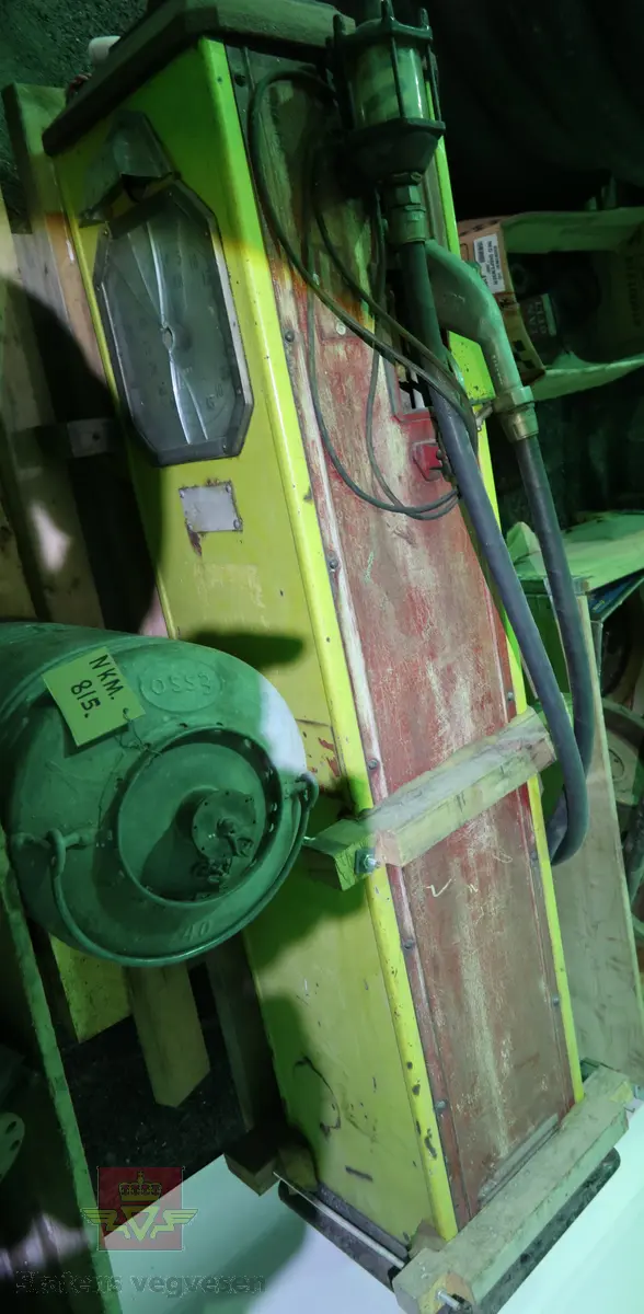 Elektrisk drevet bensinlpumpe med røde sider og gul front. Tekst: SHELL MED ICA. Pumpa har tallskive og viser som går til 100 liter. Kuppel mangler