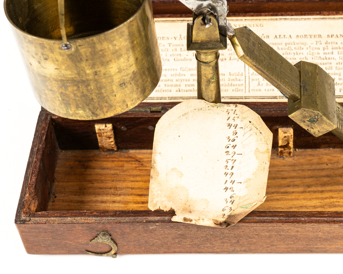 Våg av mässing, för uträkning av spannmålsvikt. Liten provvåg i fodral av trä. Måtten anger fodralets mått.