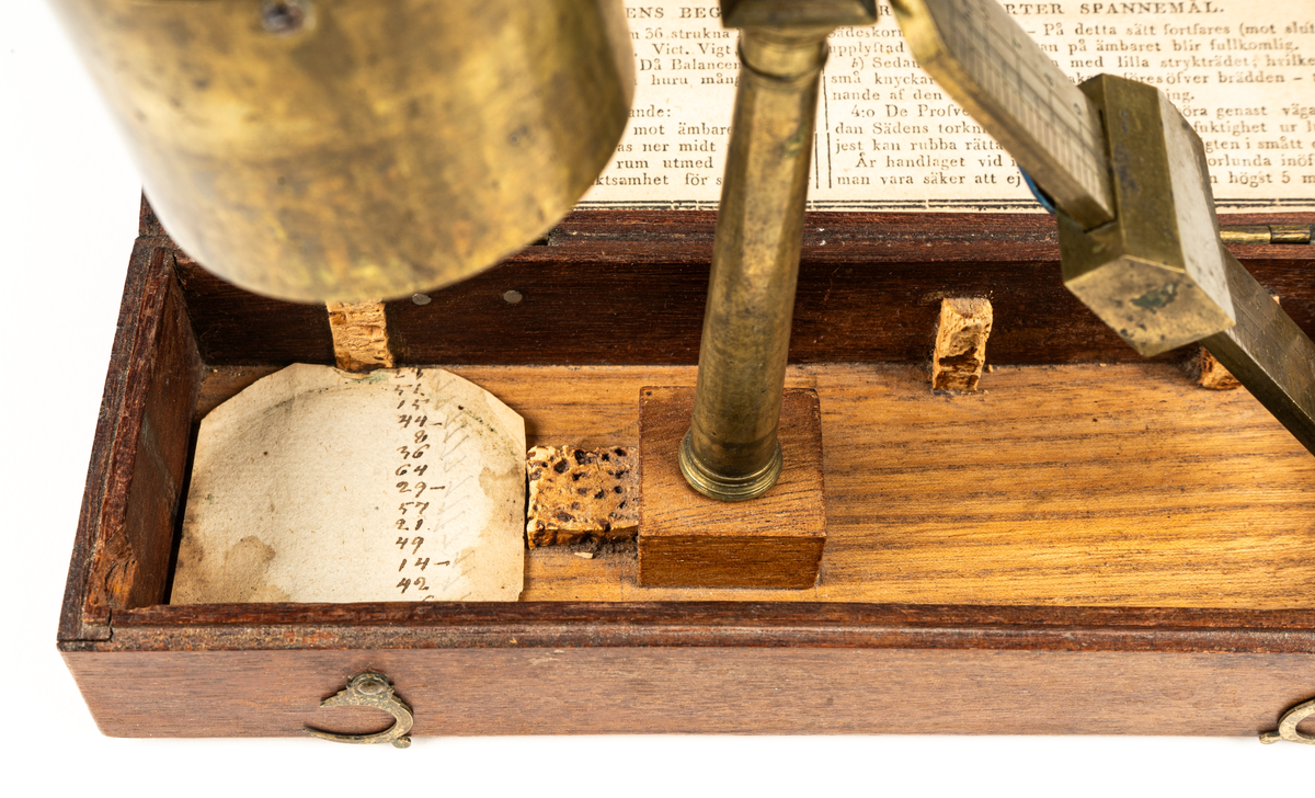 Våg av mässing, för uträkning av spannmålsvikt. Liten provvåg i fodral av trä. Måtten anger fodralets mått.