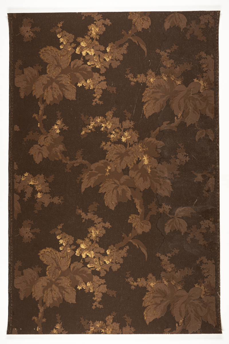 Goffrerad tapet med mönster av kraftiga blommande grenar, tryckta i två ljusbruna nyanser och guldbrons i två nyanser på mökrbrun bestruken botten.