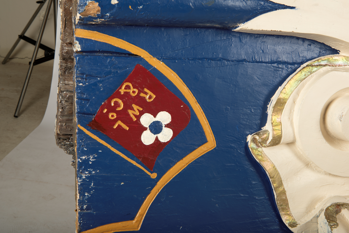 Helfigur, dame med gullrose i håret. Hvit kjole med gullkant, mørkt hår, blå sokkel med rødt emblem