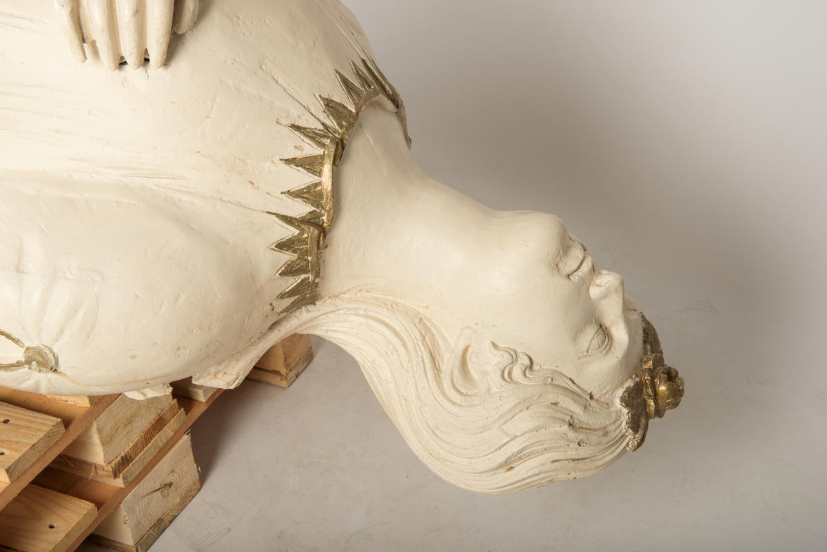 Helfigur, dame med gullrose i håret. Hvit kjole med gullkant, mørkt hår, blå sokkel med rødt emblem