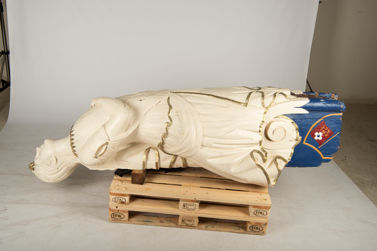 Helfigur, dame med gullrose i håret. Hvit kjole med gullkant, mørkt hår, blå sokkel med rødt emblem