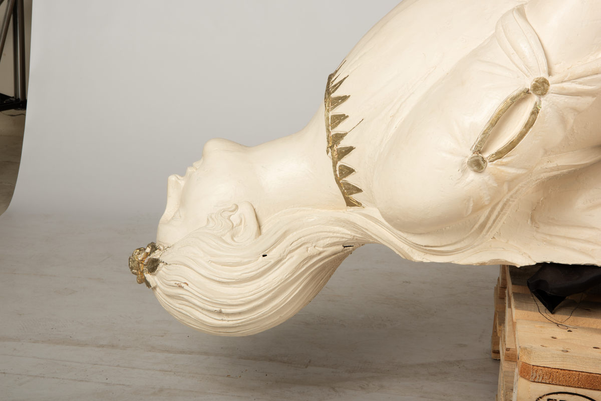 Helfigur, dame med gullrose i håret. Hvit kjole med gullkant, mørkt hår, blå sokkel med rødt emblem