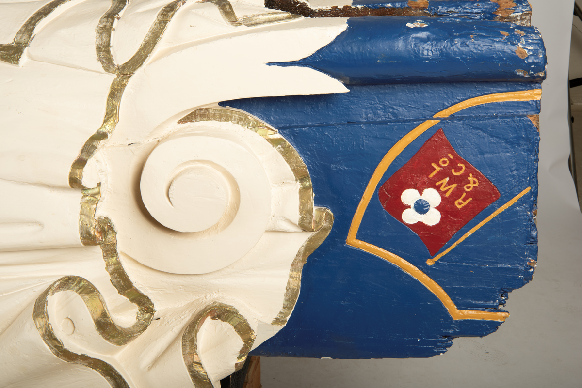 Helfigur, dame med gullrose i håret. Hvit kjole med gullkant, mørkt hår, blå sokkel med rødt emblem