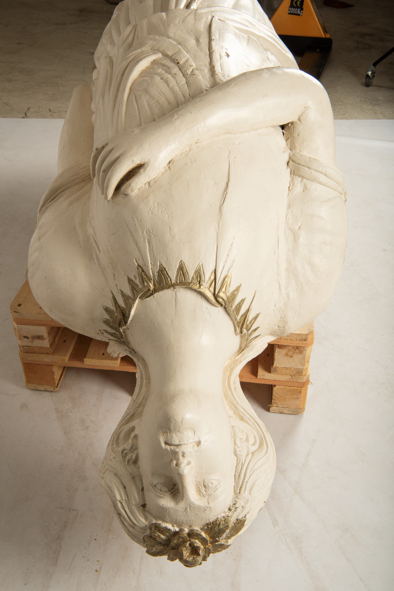 Helfigur, dame med gullrose i håret. Hvit kjole med gullkant, mørkt hår, blå sokkel med rødt emblem