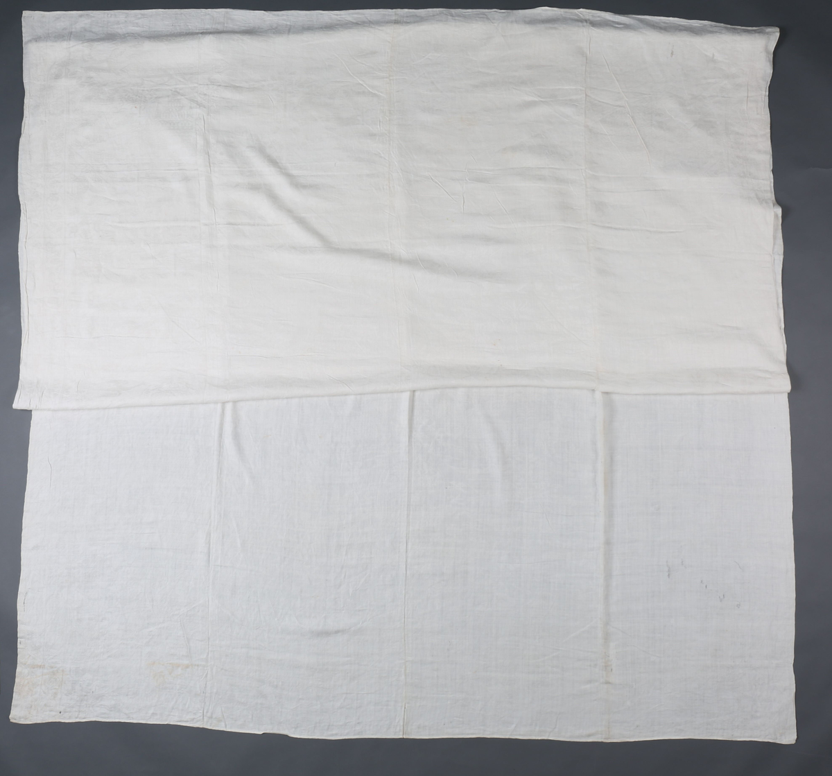 Hvit lindamask med mønster: Enhjørninger flankerer fontene stående på bakbenene med liggende hjerter og andre dyr omkring. Damer til hest med hatt på hodet. Duken har smal fall på kortsidene.