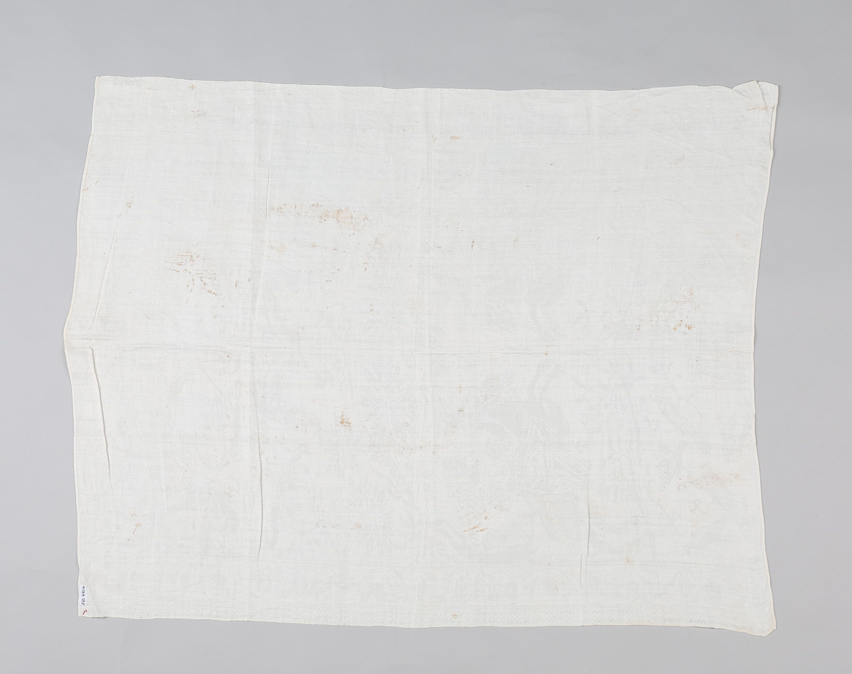 Hvit lindamask med mønster: damer til hest med jaktfalk, hornblåsende jegere med hunder, blomstermønster samt enkeltbord på langsidene. Smal fall på kortsidene. Merket med liten rød stjerne.