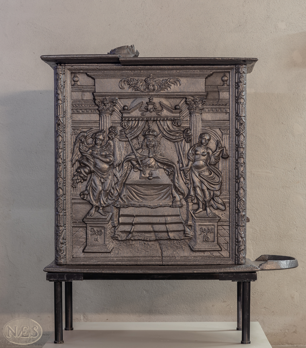 En rektangulær kasseovn med åpning på kortsiden. På langsiden - gjengivelse av tittelbladet til Christian V sin norske lov. På arkitraven over tronstolen C 6 i kronet speilmonogram mellom palmegrener. På de allegoriske figurenes (Overflødighetsgudinnen og Justitia) postamenter Christian VI sitt valgspråk. Faste skinner med geometrisk ornamentikk.
Øverst på kortsiden de forenede rikers våpen omgitt av elefantordens kjede. Nederst påskrift omgitt i en kartusj.