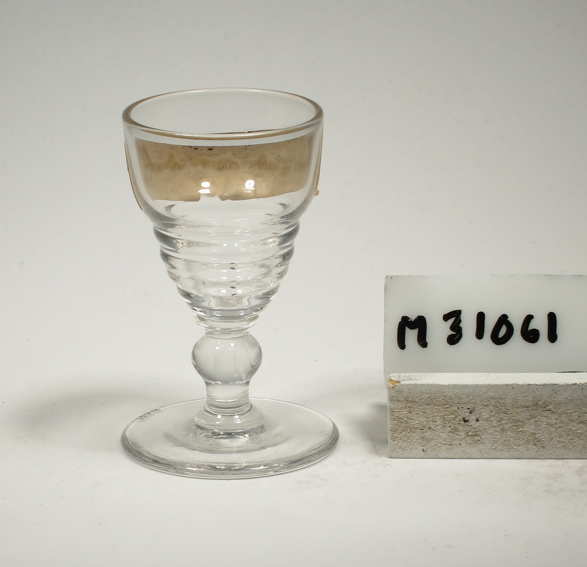 Formgivare: Ingrid Atterberg. Likörglas på ben och fot. Ovoid kupa med horisontella vulster på nedre delen. Pelarben.